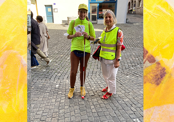 Tag des Weissen Stockes Aktion in Zürich - Blindversuche. Zwei aktive betroffene Frauen in gelben Westen und eine davon mit gelbem Blindenbund-Käppi und Weissem Stock posieren in der Innenstadt Zürich.
